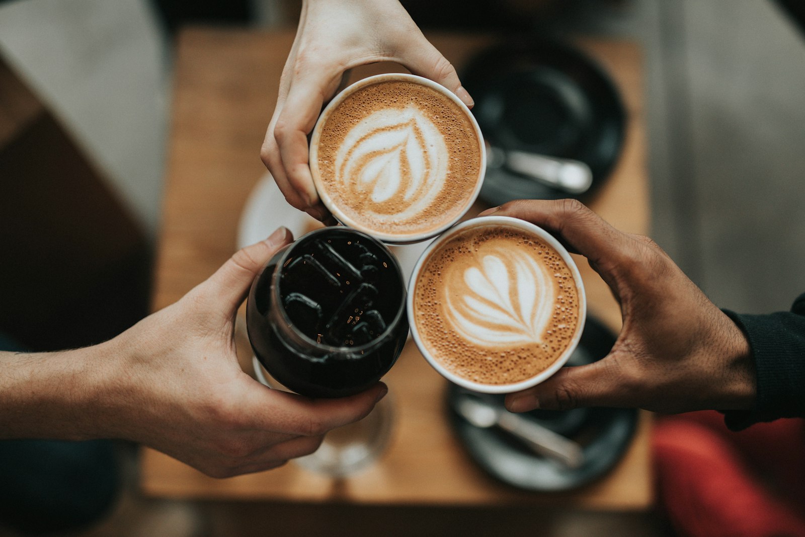 Three people toasting with coffee cups over a café table